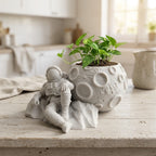 CONQR astronaut moon planter with a money plant on a pale wooden kitchen table